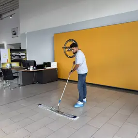 Ein Mitarbeiter reinigt den Boden in einem modernen Opel Autohaus mit gelber Wand und Opel-Logo.