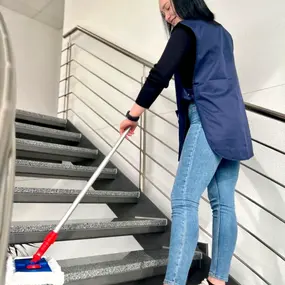 Eine Frau reinigt mit einem Wischmopp eine Treppe in einem modernen Treppenhaus.