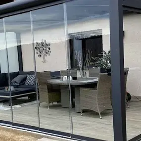 Moderner Wintergarten mit Glaswänden, gemütlicher Sitzecke und Esstisch auf Holzboden im Garten.