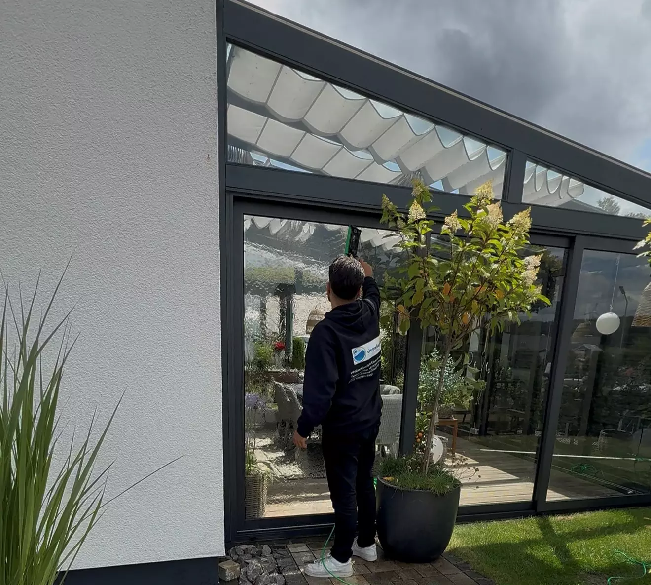 Ein Mann reinigt eine große Glasfront an einem modernen Wintergarten mit professioneller Fensterreinigung.